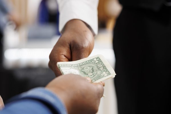 Close up of male African American waiter receiving tip from generous hotel guest. Tourist giving money cash to restaurant worker, making order, paying bill. Tipping in hospitality industry